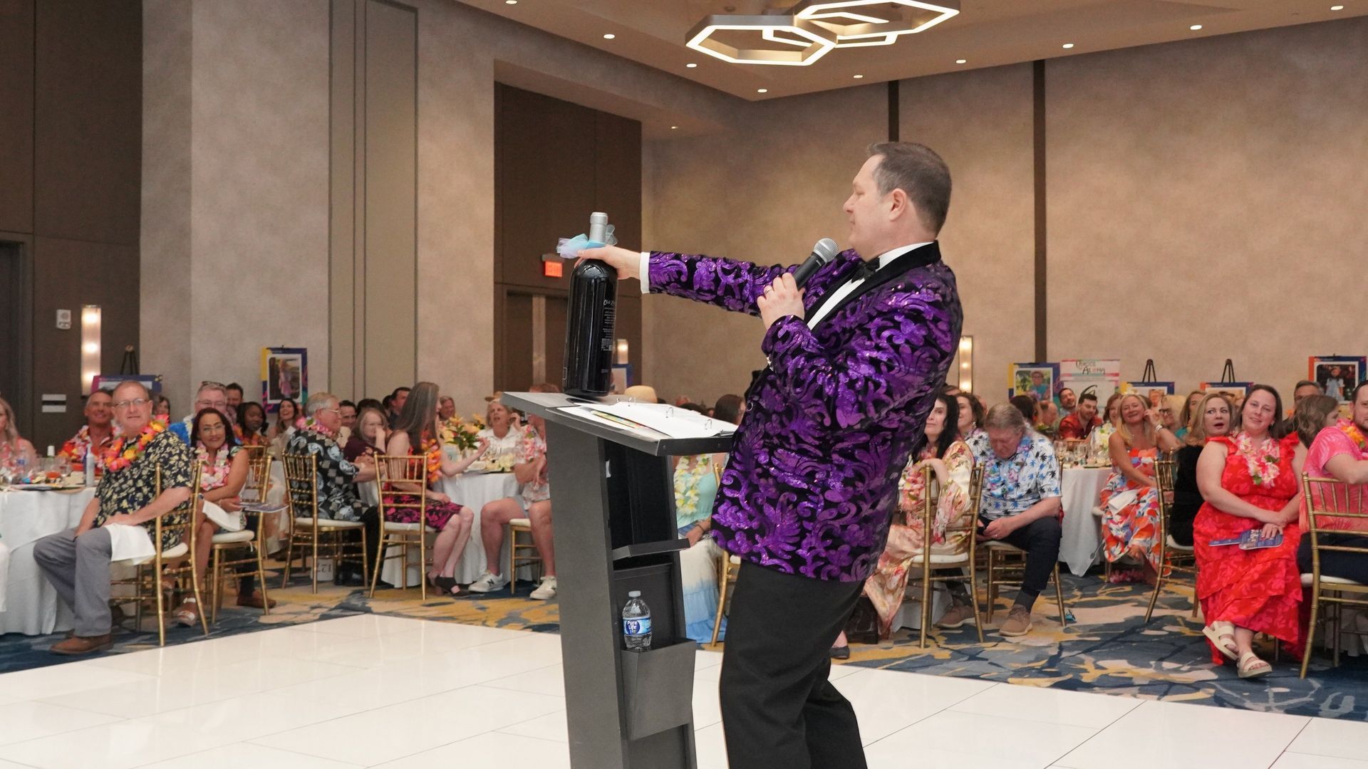 Speaker in purple jacket addressing an audience at a banquet hall podium