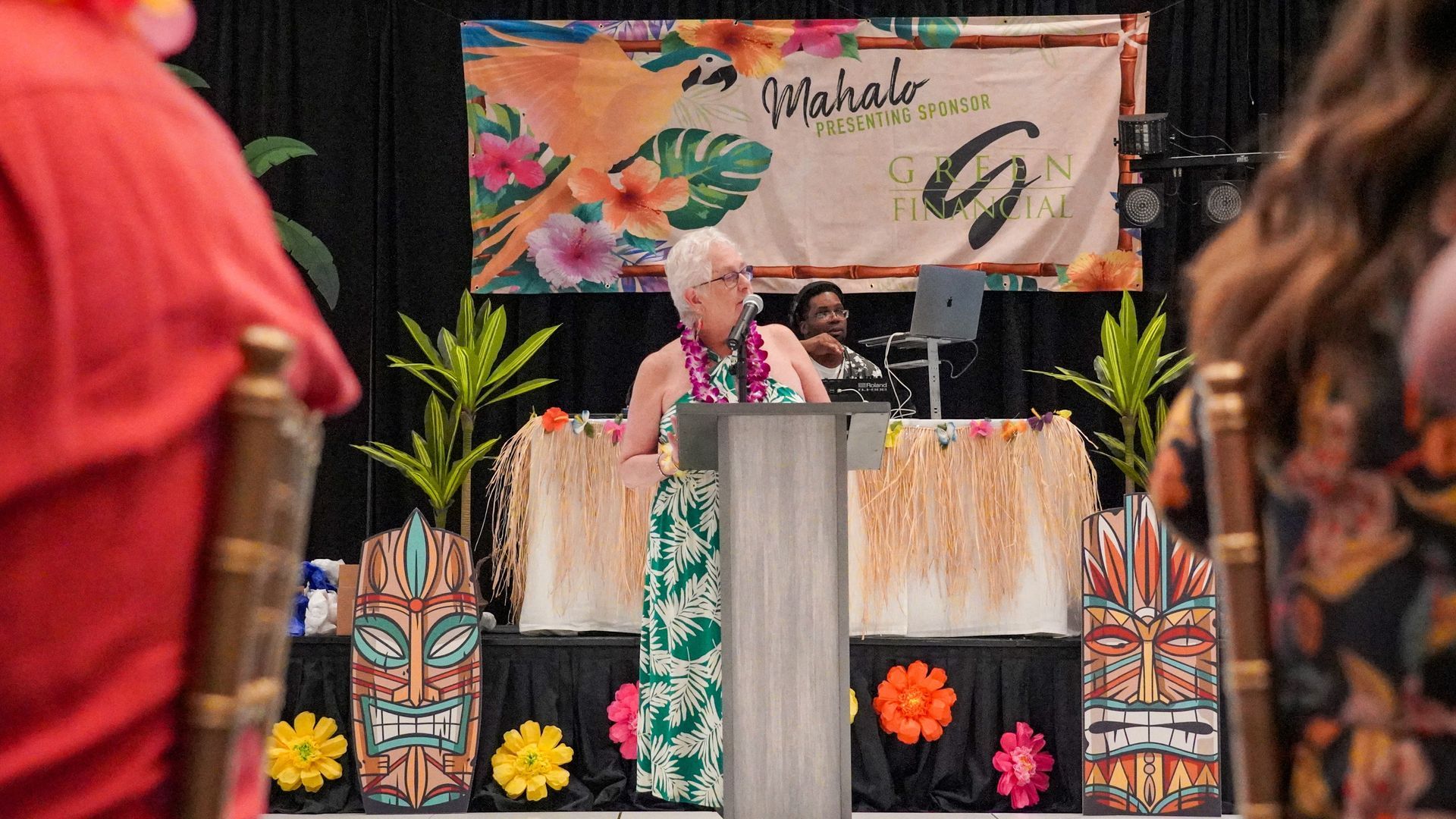 Person at a decorated podium on a floral stage with a banner backdrop and colorful Mexican folk art accents