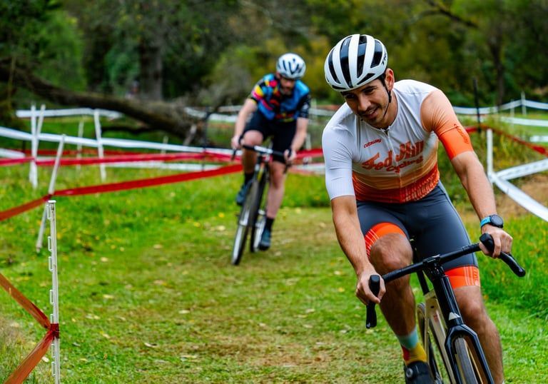 Two cyclists racing around a grassy bend, front rider in white and orange jersey leaning into the turn