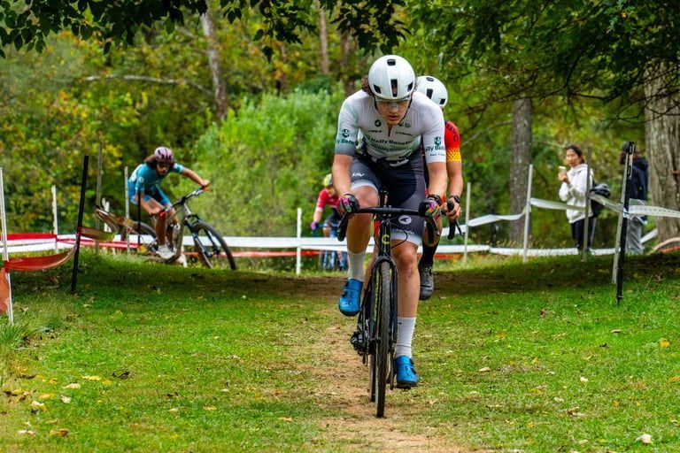 Cyclists racing on a grassy outdoor course, with one rider in white leading.