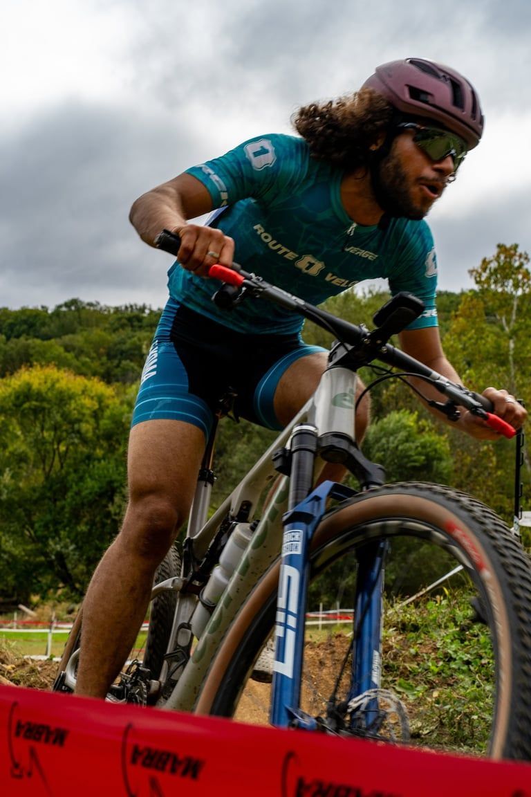 Cyclist in teal gear riding a mountain bike over a red barrier outdoors under cloudy skies