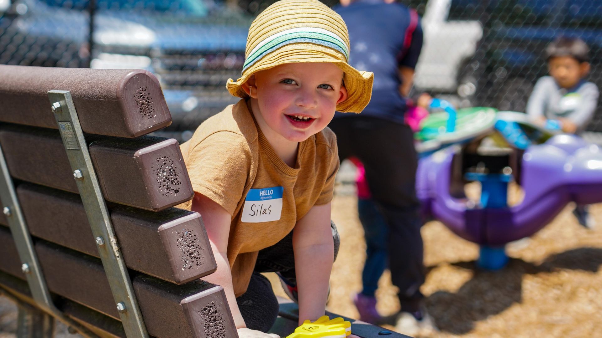 Smiling child in a straw hat leaning on a wooden bench at a sunny outdoor event