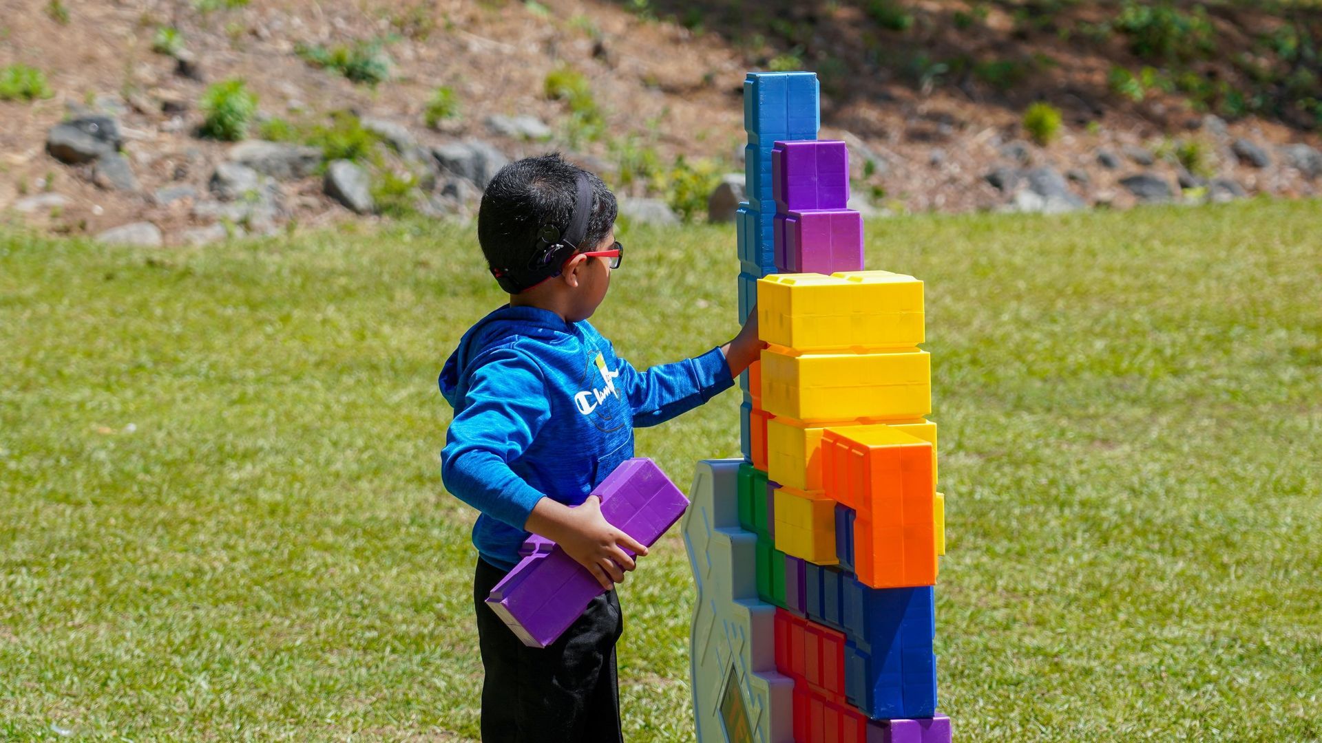 Child stacking colorful toy blocks on a vertical wall outdoors on grass