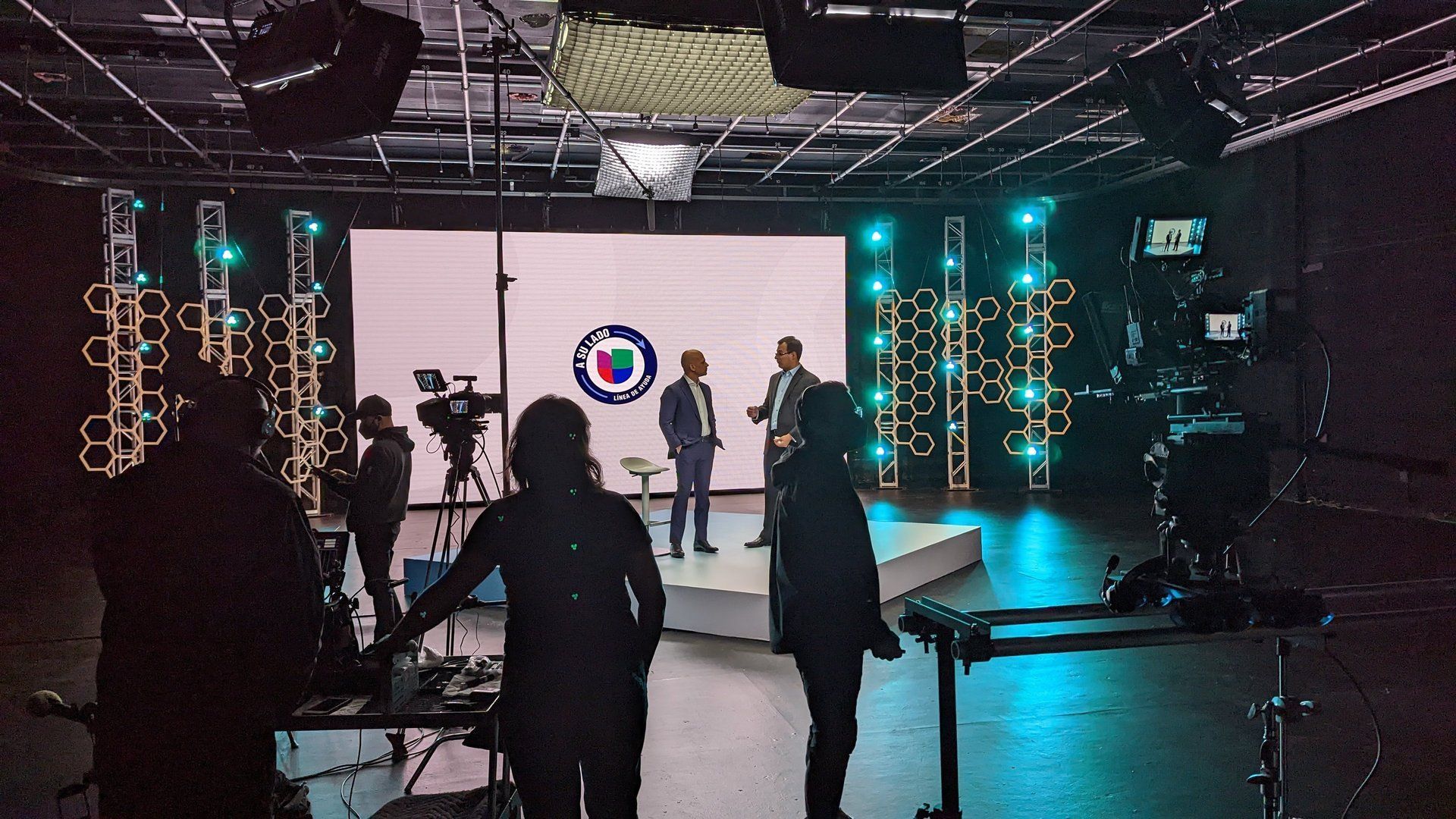 Film set with crew filming people on a stage lit by teal and magenta lights