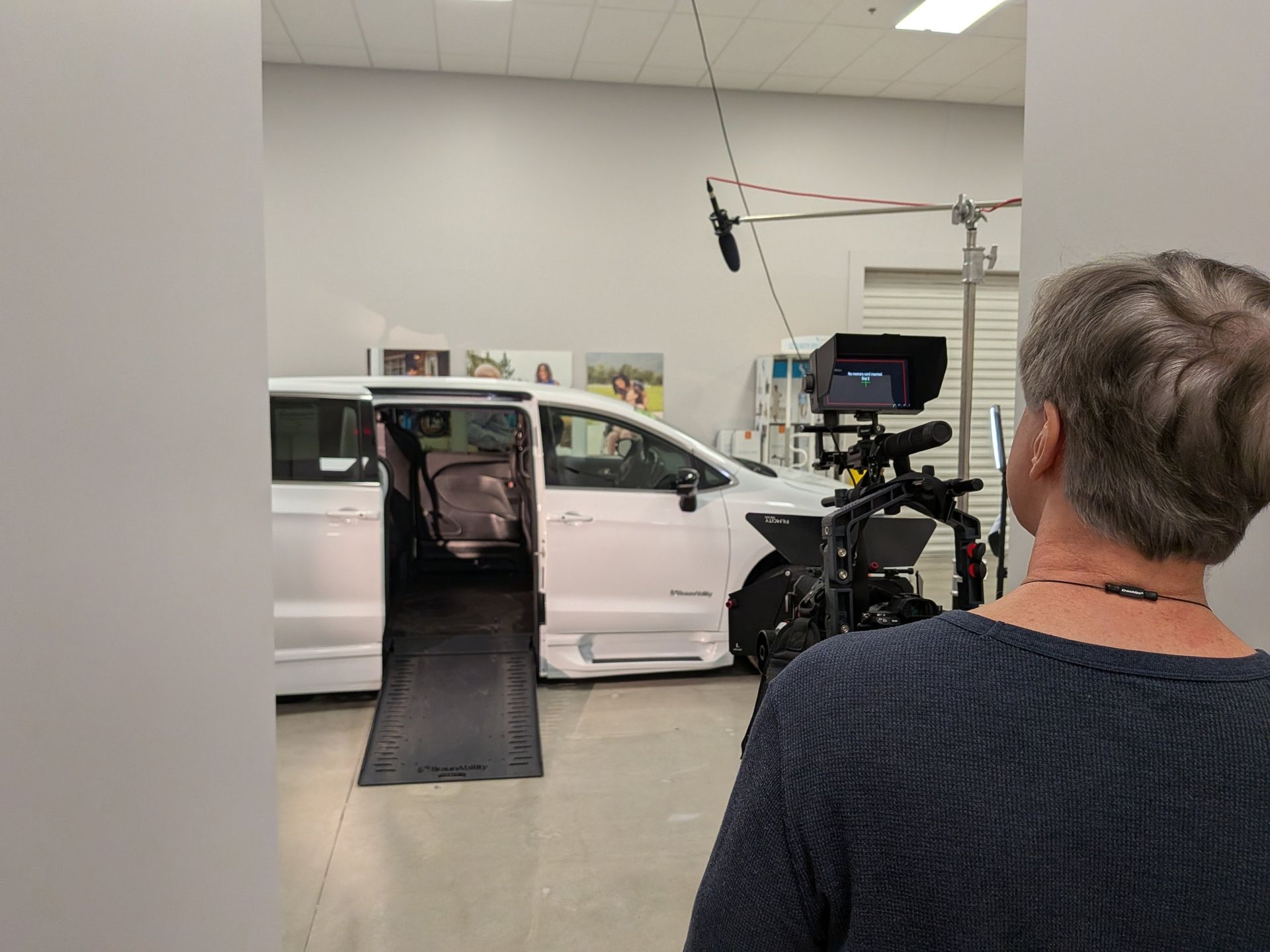 White van in a studio with its side door open and a ramp extended, filmed by a camera crew.