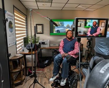 Man seated in a recording studio, speaking on camera with monitors and lighting equipment around him