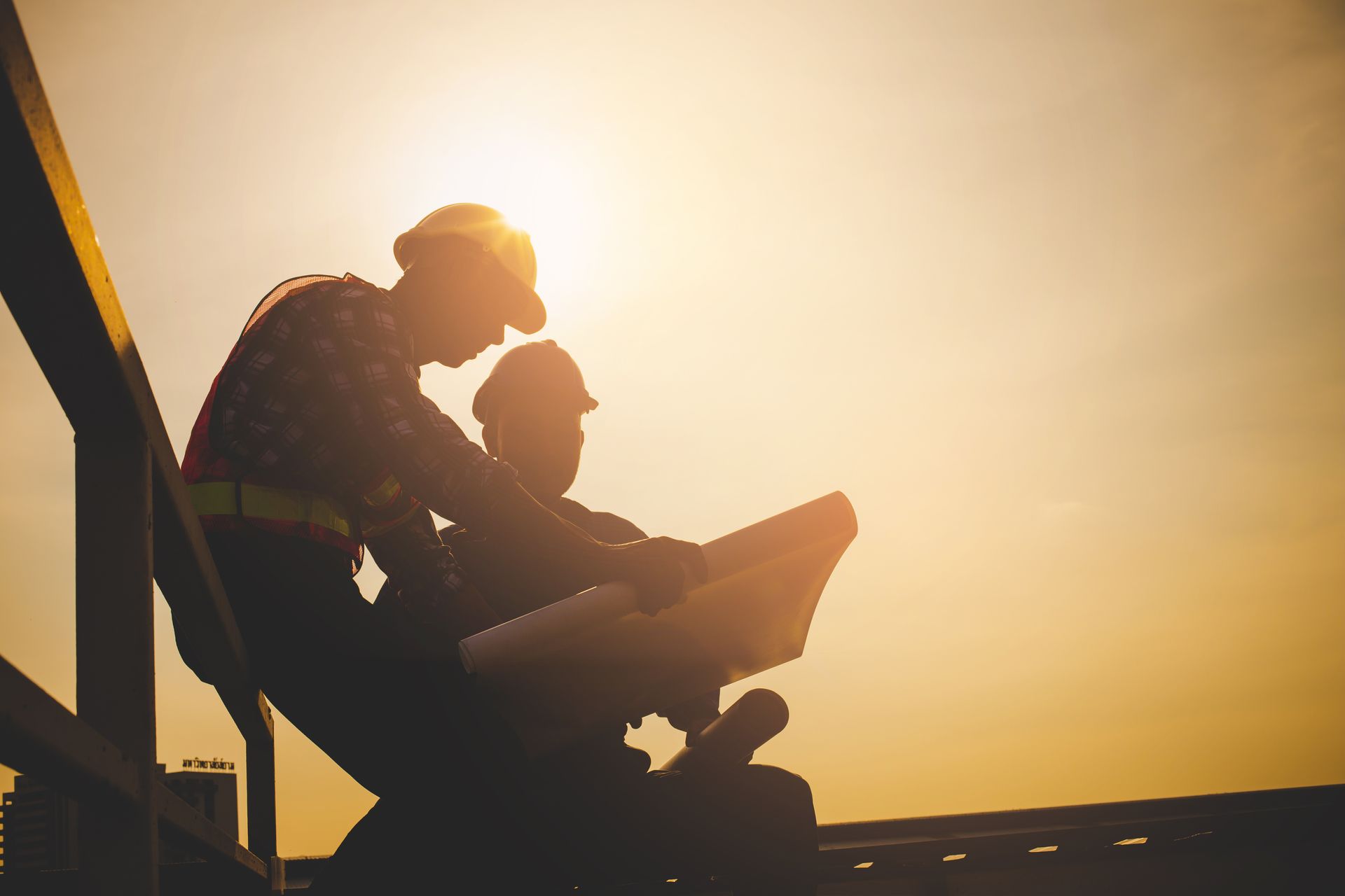 The silhouette of two general contractors as they check on the blueprints of a project. The silhouette of two general contractors as they check on the blueprints of a project.