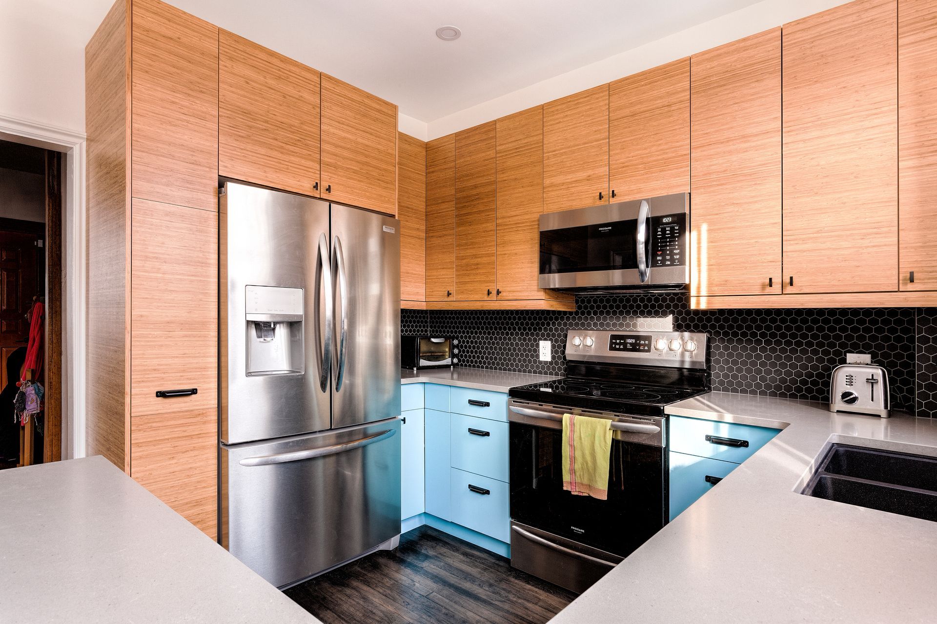 A modern kitchen featuring natural wood upper cabinets, light blue lower cabinets, a stainless steel fridge, and oven.