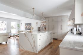 A bright, open-concept kitchen with a large marble-topped island, light cabinetry, and hardwood floors.