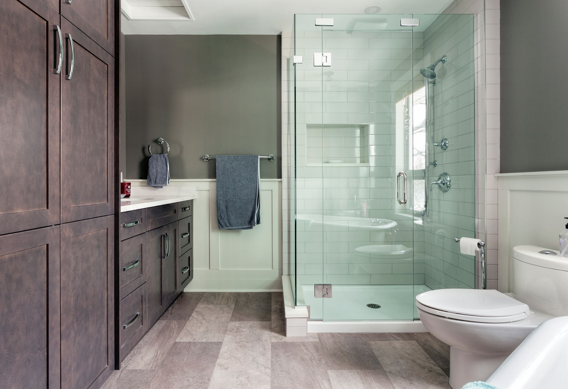A modern bathroom featuring a dark wood vanity, a glass-enclosed walk-in shower, a toilet, and light-colored flooring.