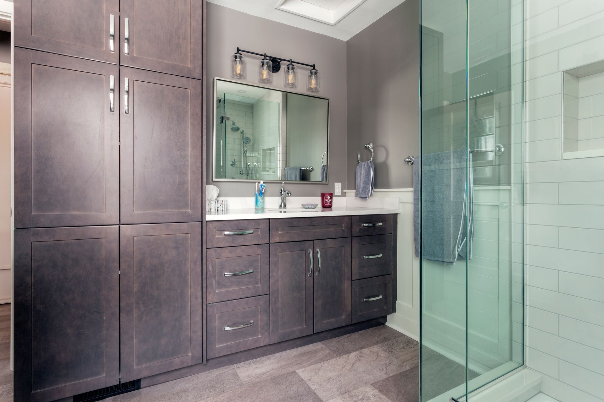 A modern bathroom featuring dark wood cabinetry, a vanity with a mirror and lighting, and a glass-enclosed shower.