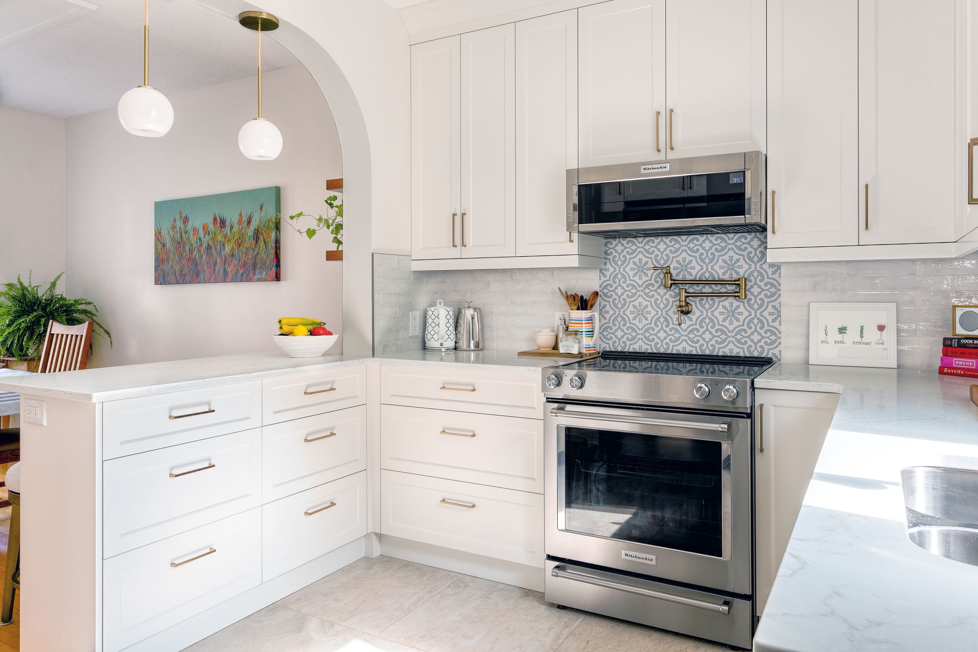 A bright, modern kitchen featuring white shaker cabinets, a stainless steel range, and a blue herringbone tiled backsplash.