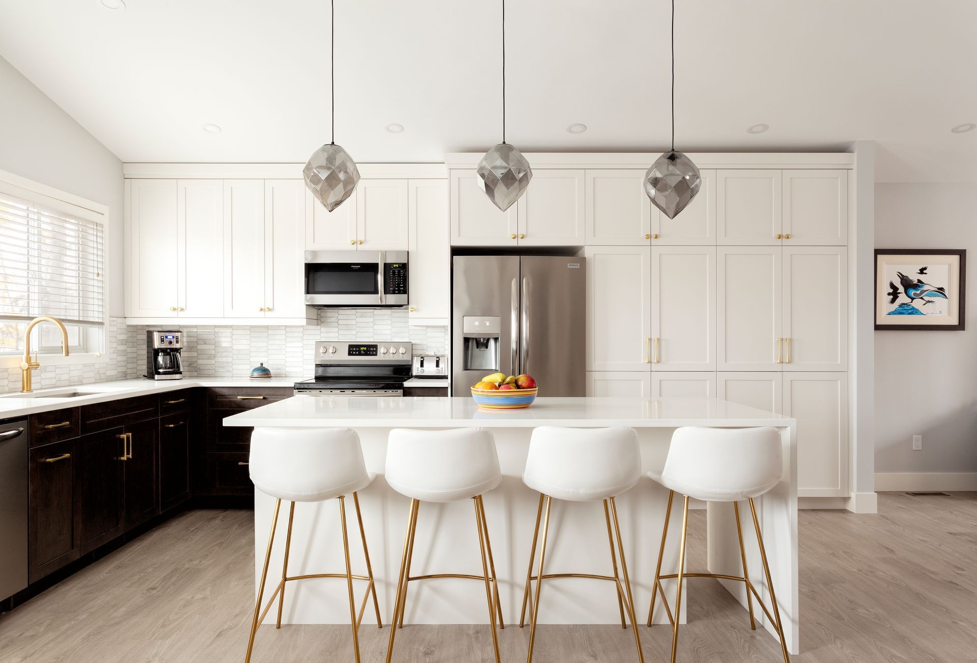 A modern kitchen with a white quartz island, four white bar stools with gold legs, dark cabinets, and white upper cabinets.