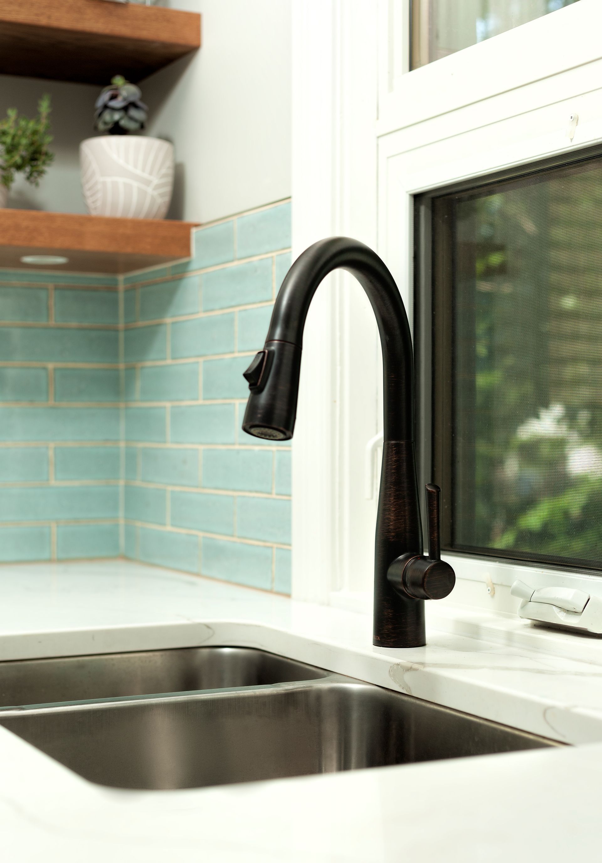 A matte black pull-down kitchen faucet sits at a white countertop sink against a light blue tiled backsplash.