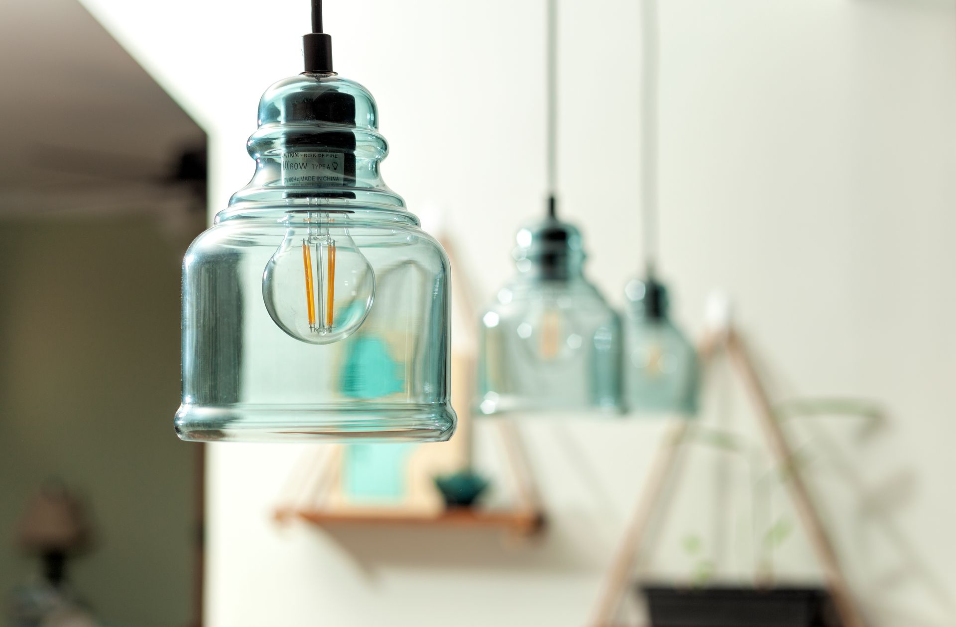 Three blue glass pendant lights hang in a row in a softly lit, blurred interior setting.