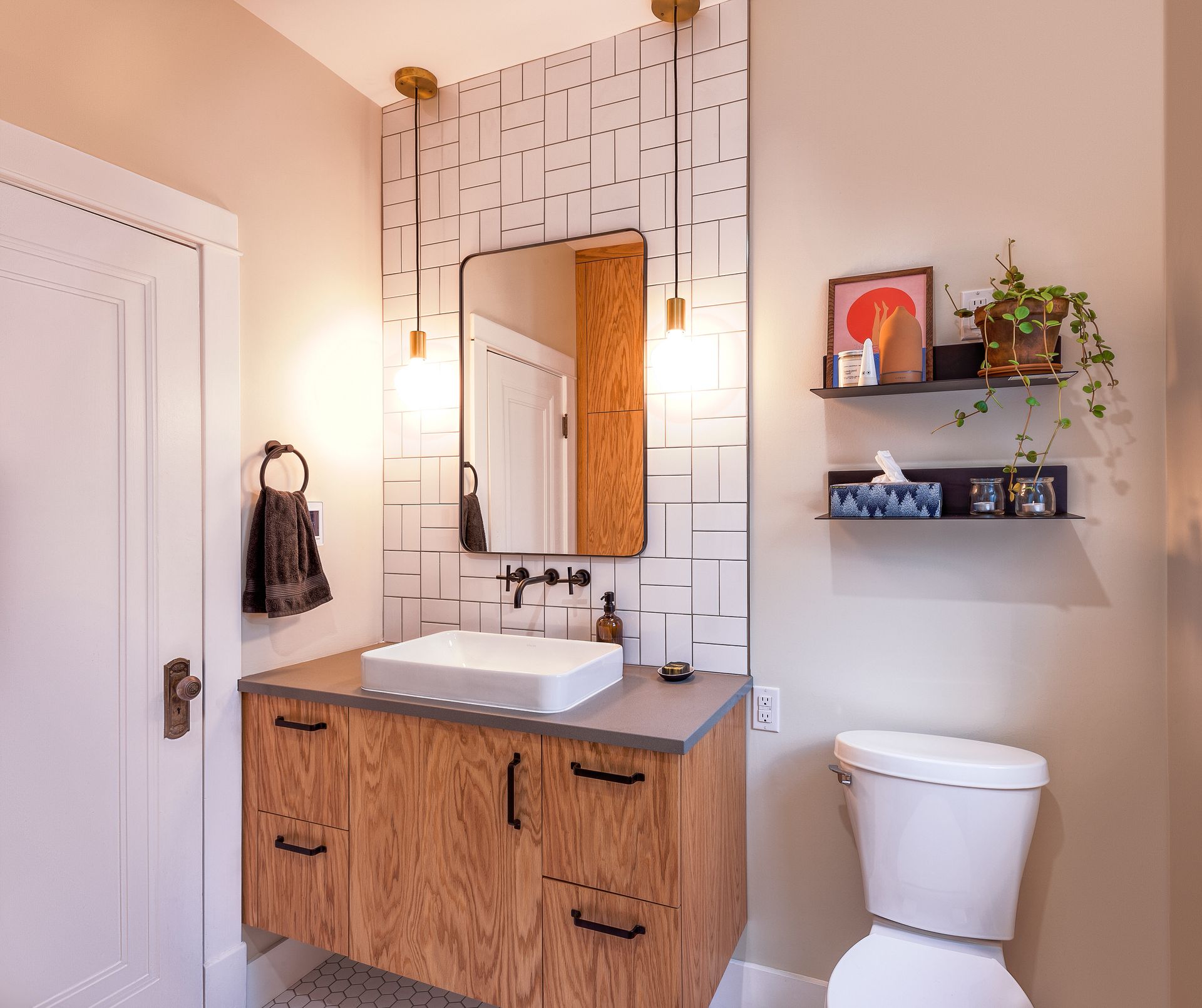 A modern bathroom with a wood-veneer vanity, white vessel sink, rectangular mirror, and white geometric tile backsplash.