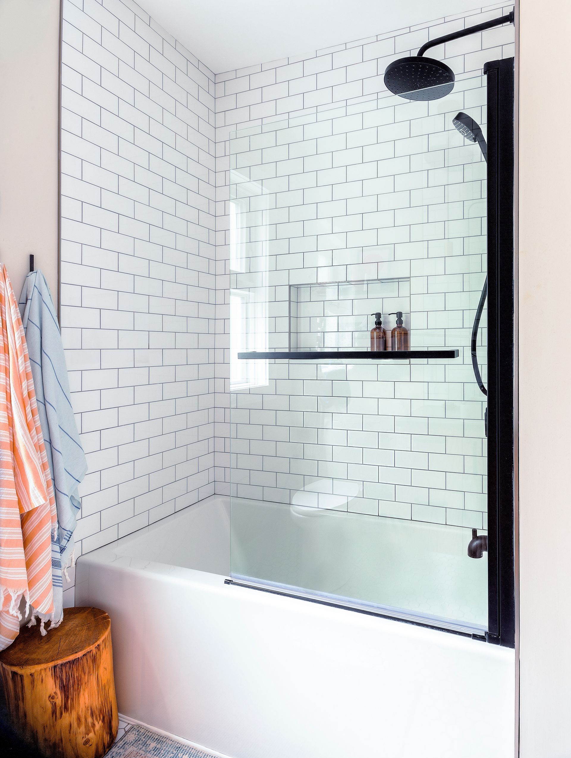 A bathtub with a glass shower screen, matte black fixtures, and white wall tiles featuring a black geometric pattern.