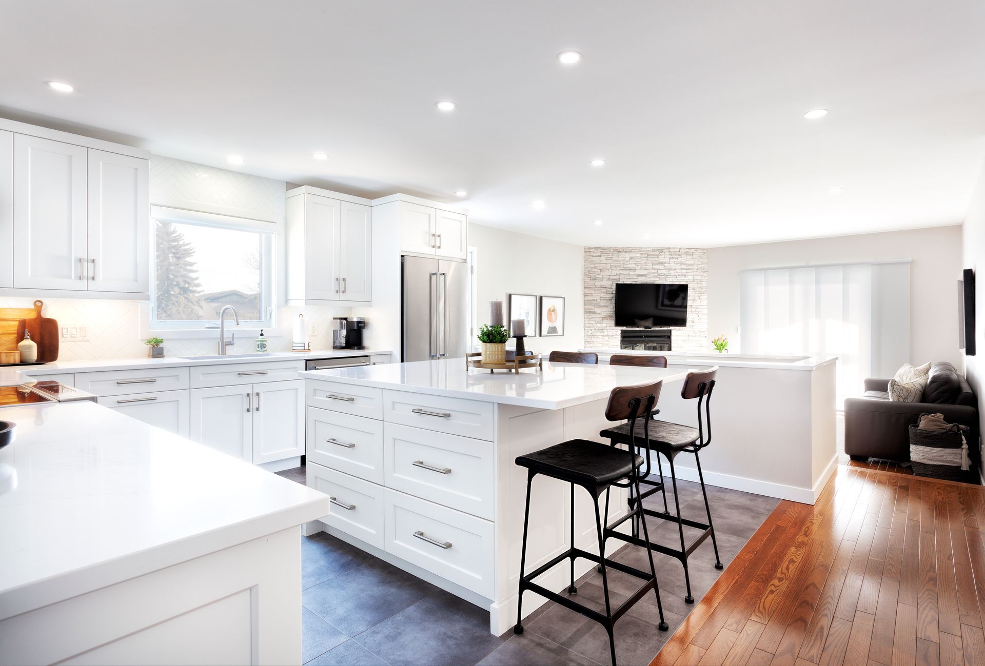a kitchen with white cabinets , a large island , stools and a refrigerator .