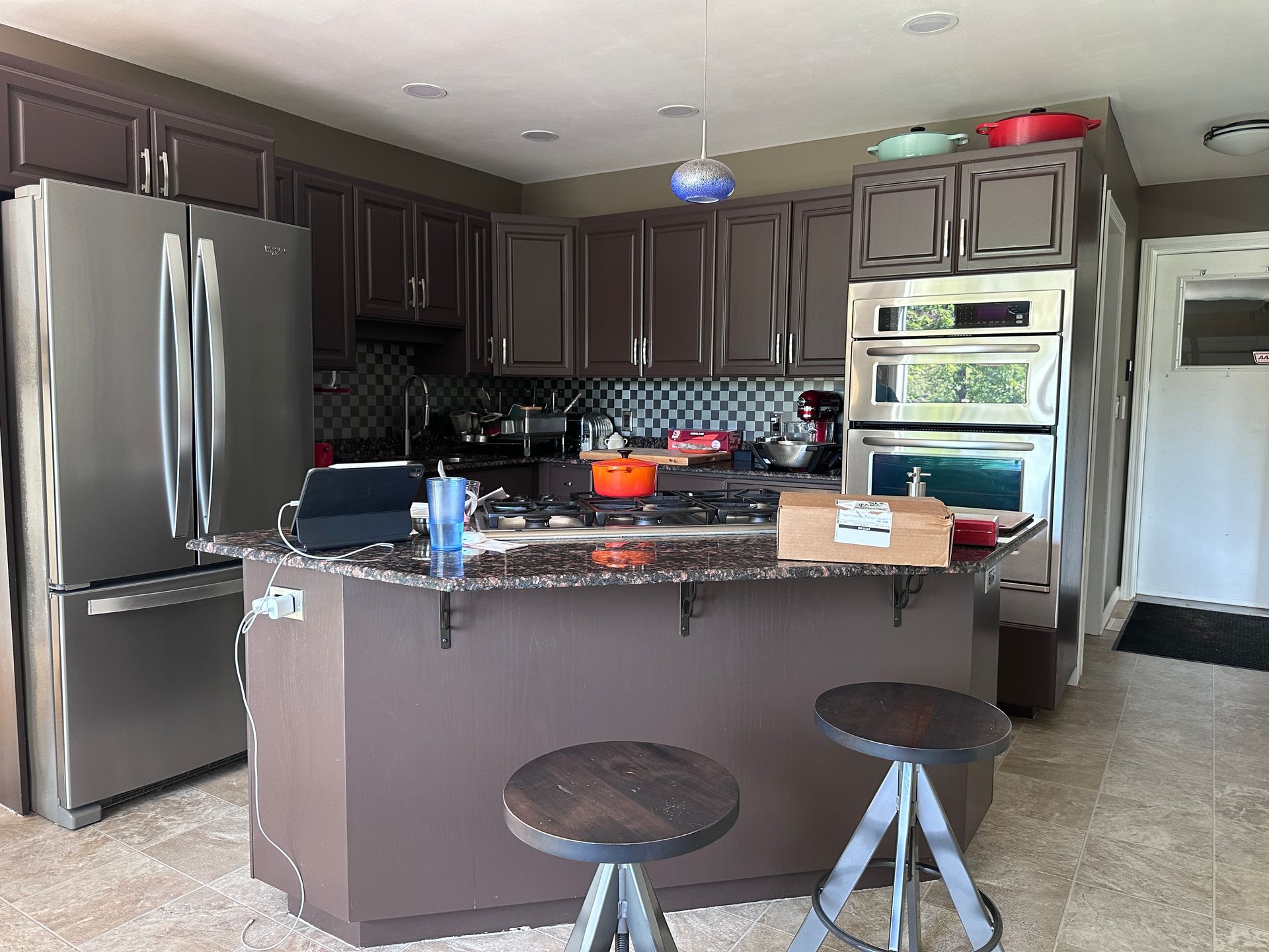 A kitchen with stools , a refrigerator , a stove , a microwave , and a large island.