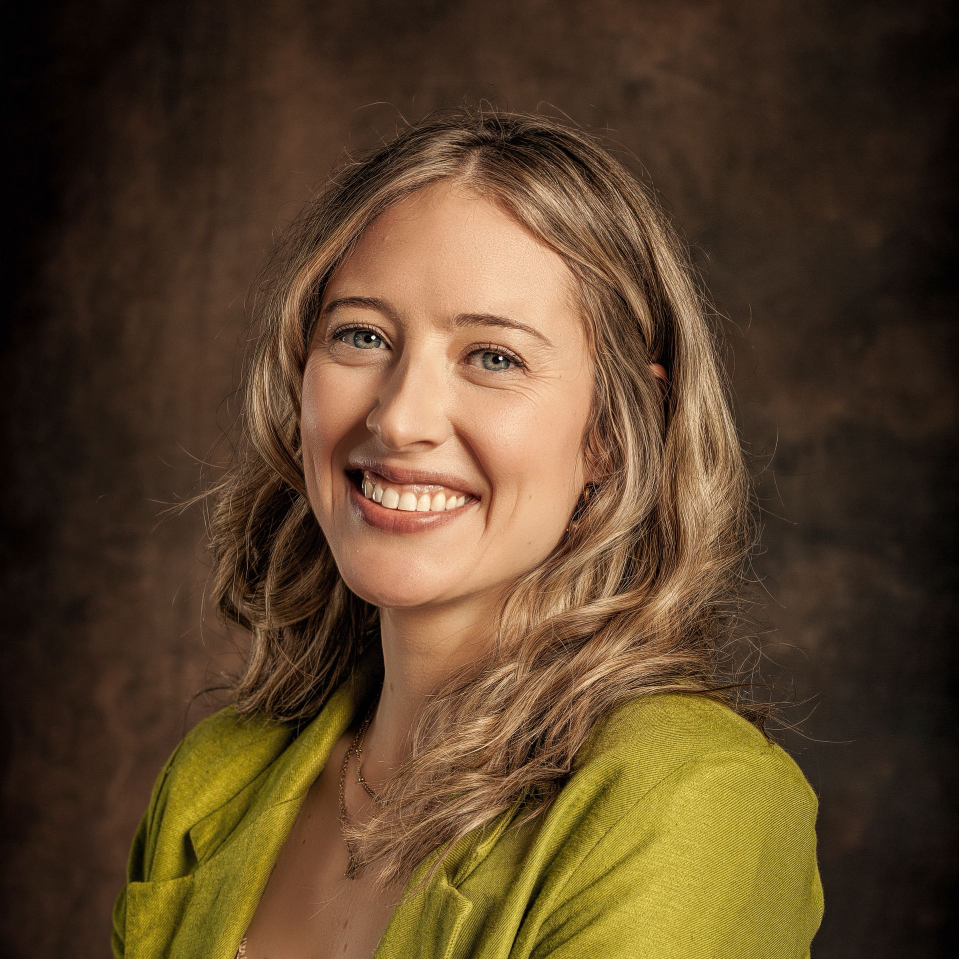 Smiling woman in a green top against a dark studio backdrop
