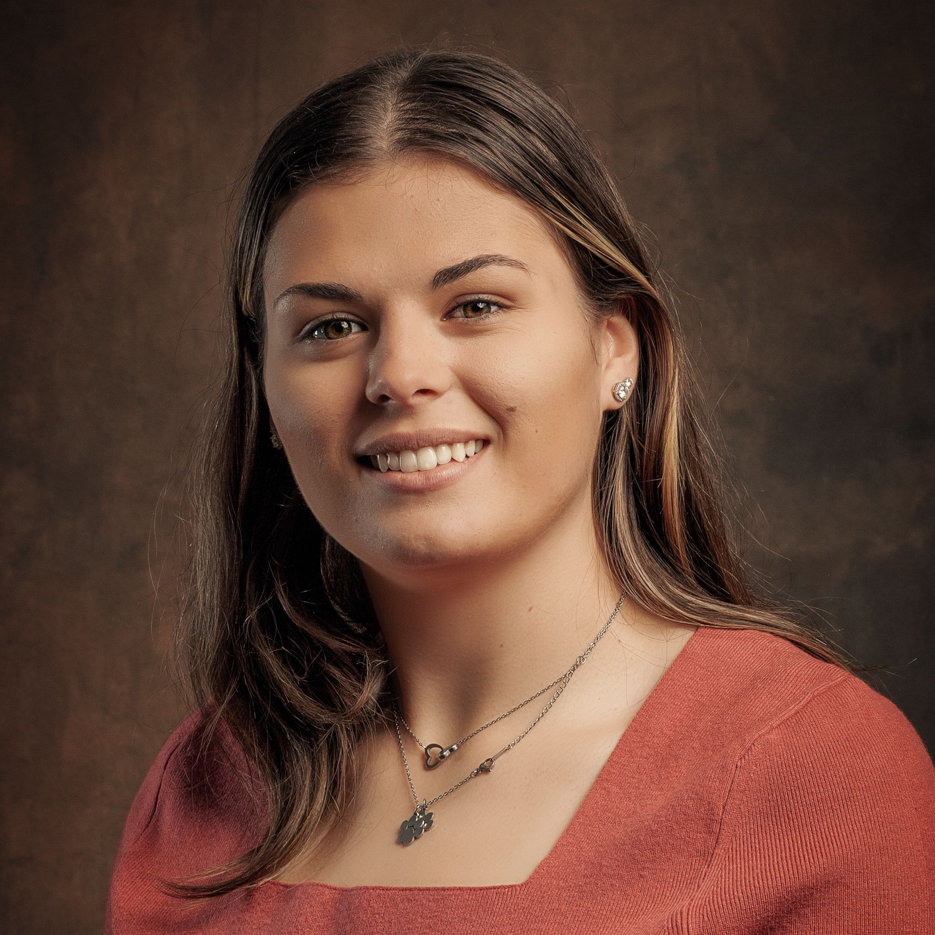 Studio portrait of a smiling person in a red top against a dark background