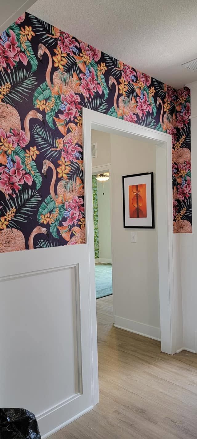 Hallway with bold floral wallpaper, white trim, and an open doorway to a room with framed wall art.