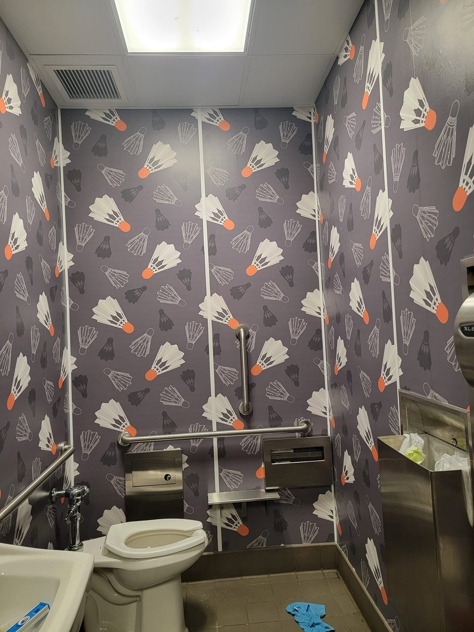Small bathroom with dark floral wallpaper, toilet, sink, and a vanity with cleaning supplies.