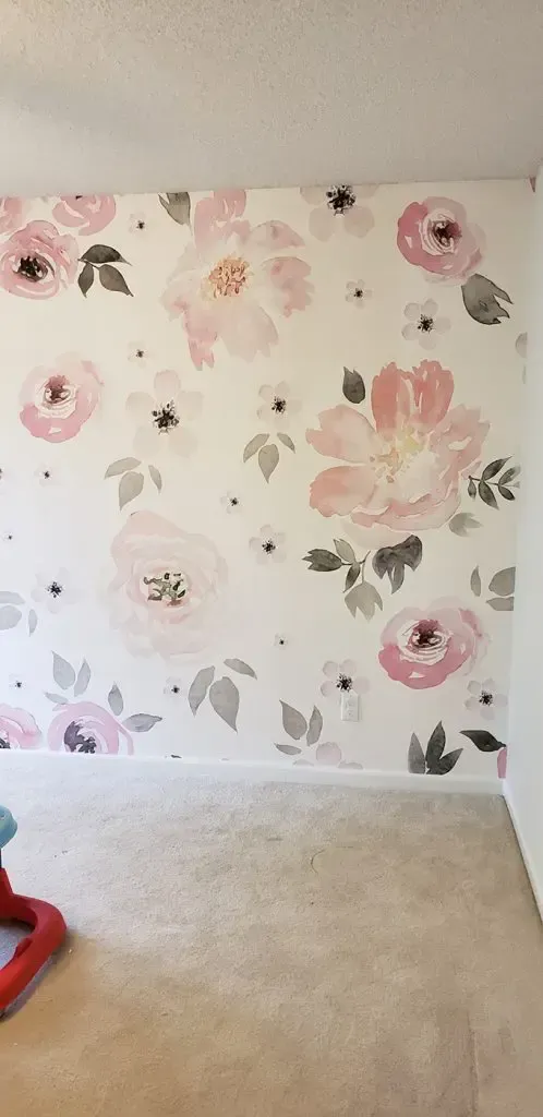 Empty room with beige carpet and pink floral wallpaper, with a red vacuum partially visible in the corner