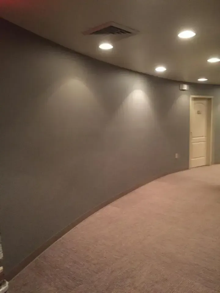 Curved gray hallway with recessed ceiling lights and a beige door at the end.
