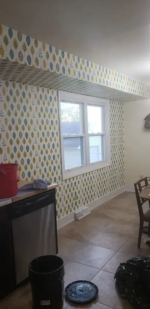 Small kitchen with patterned wallpaper, tiled floor, window, and a trash bin near a counter.