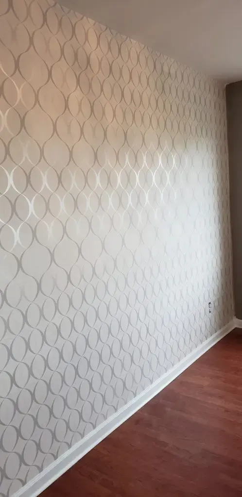 White patterned wallpapered wall beside a wood floor in a narrow room or hallway