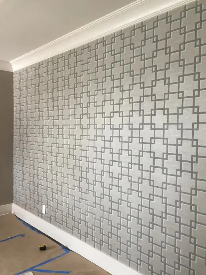 Empty room with gray patterned wallpaper, white trim, and protective floor covering during renovation