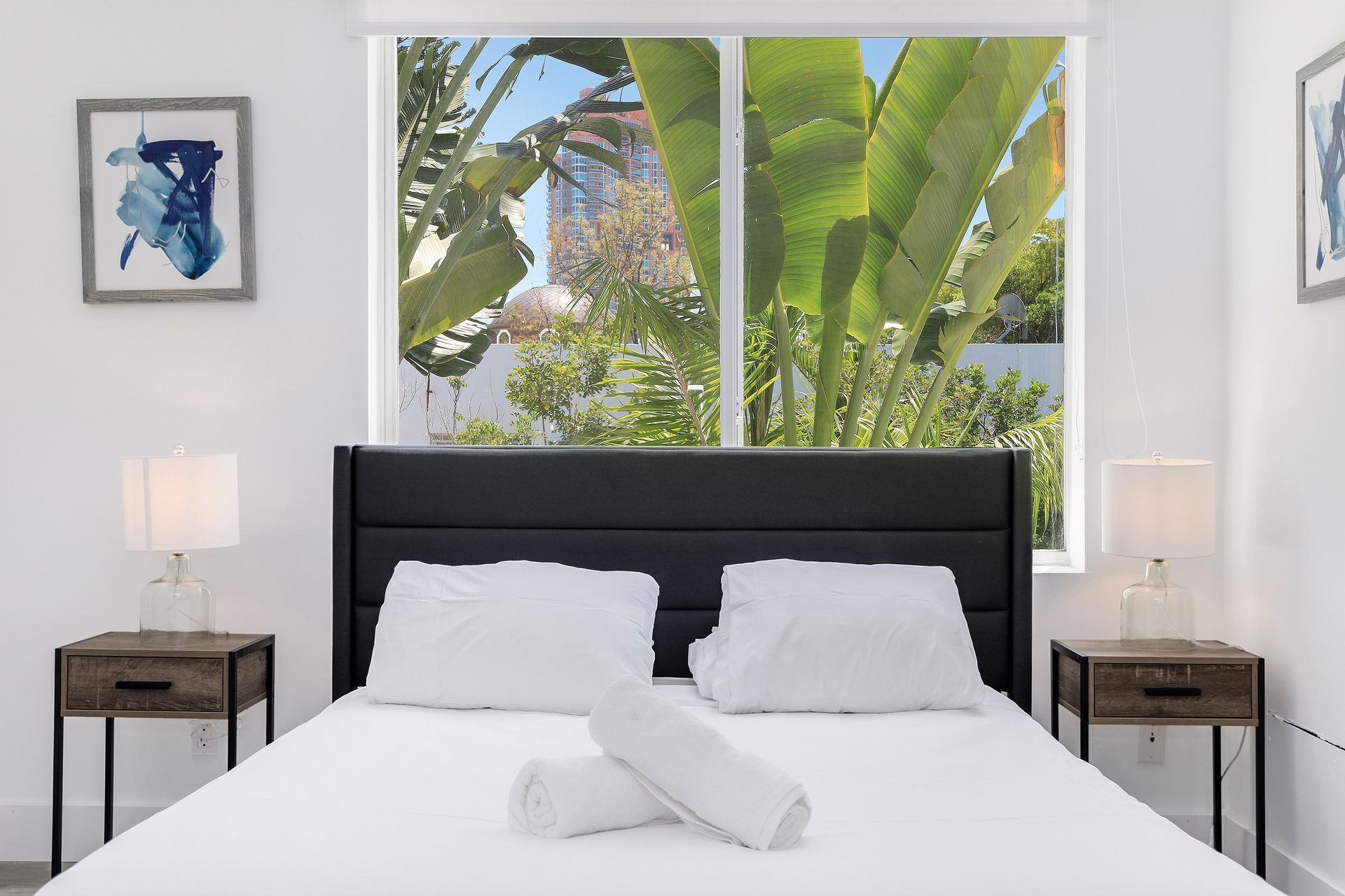 Bedroom with a black headboard, two nightstands, and a window with a view of greenery.