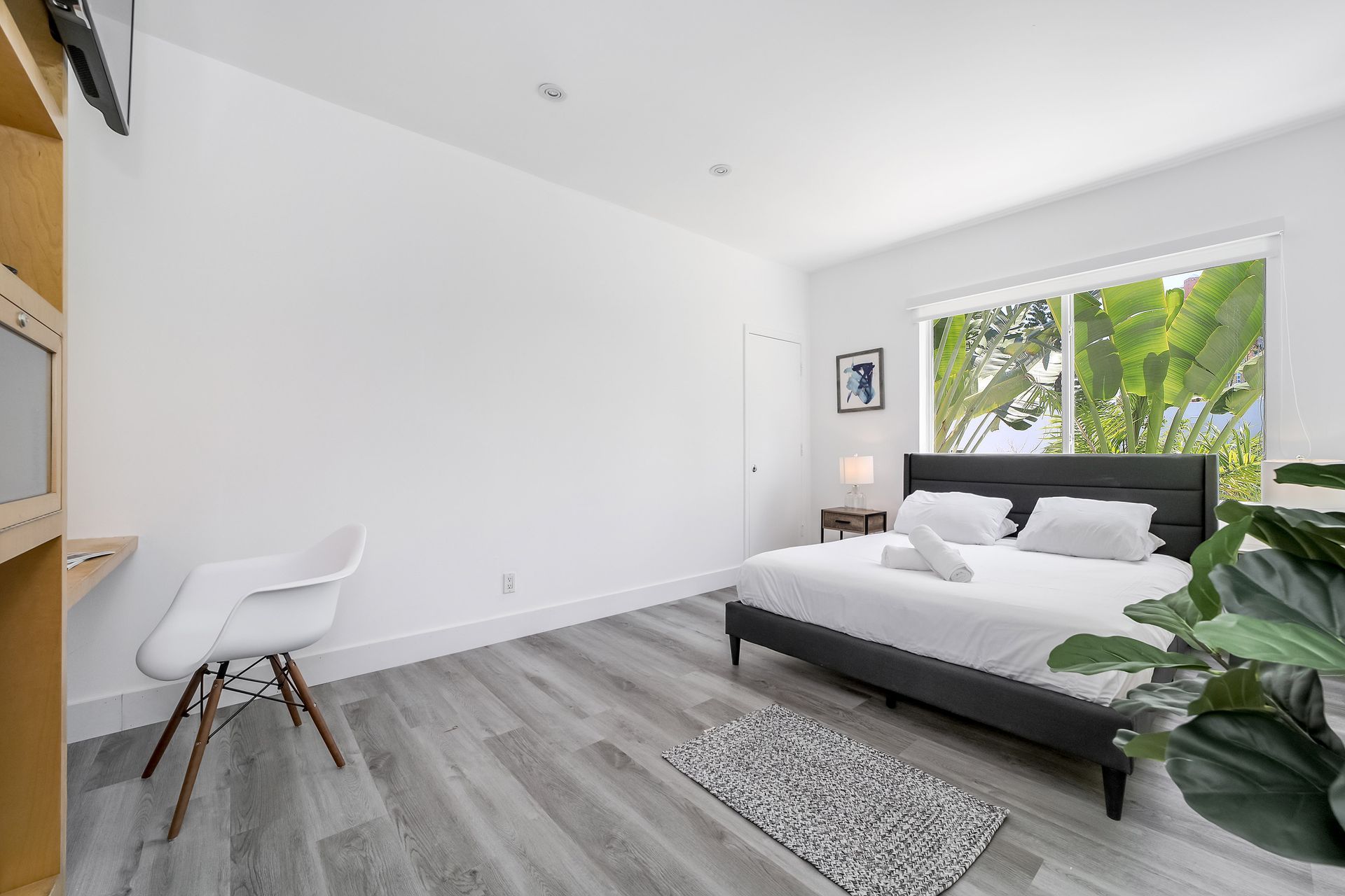 Bedroom with a bed, desk, and large window overlooking greenery. Gray and white color scheme.