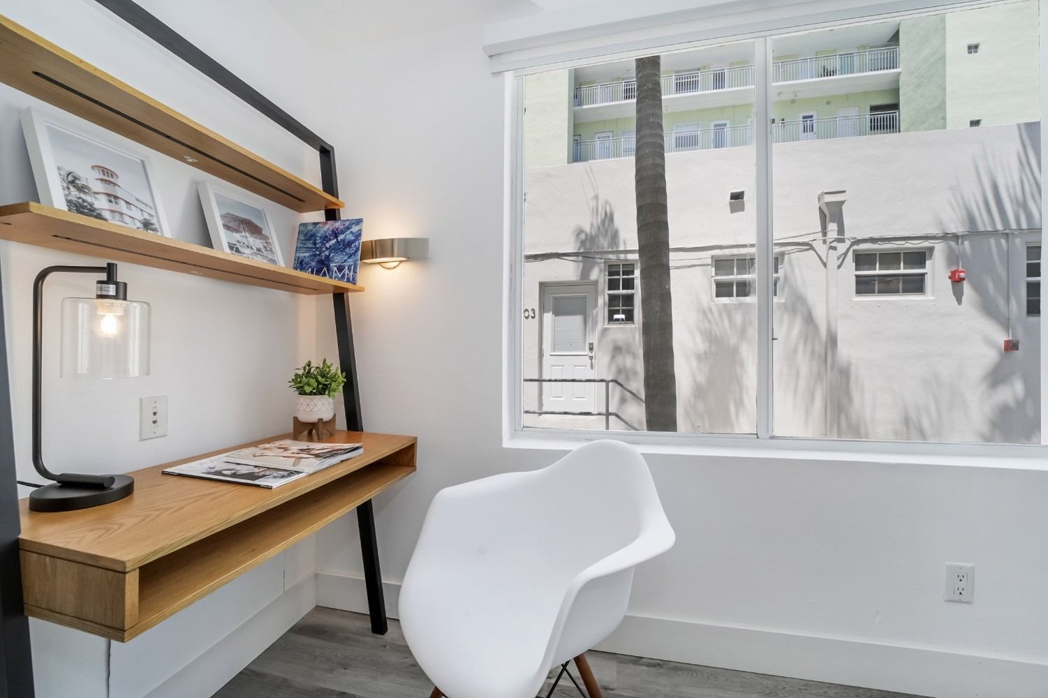 Desk with shelves, chair, and window. White walls, wood desk, and black metal accents in a modern office.