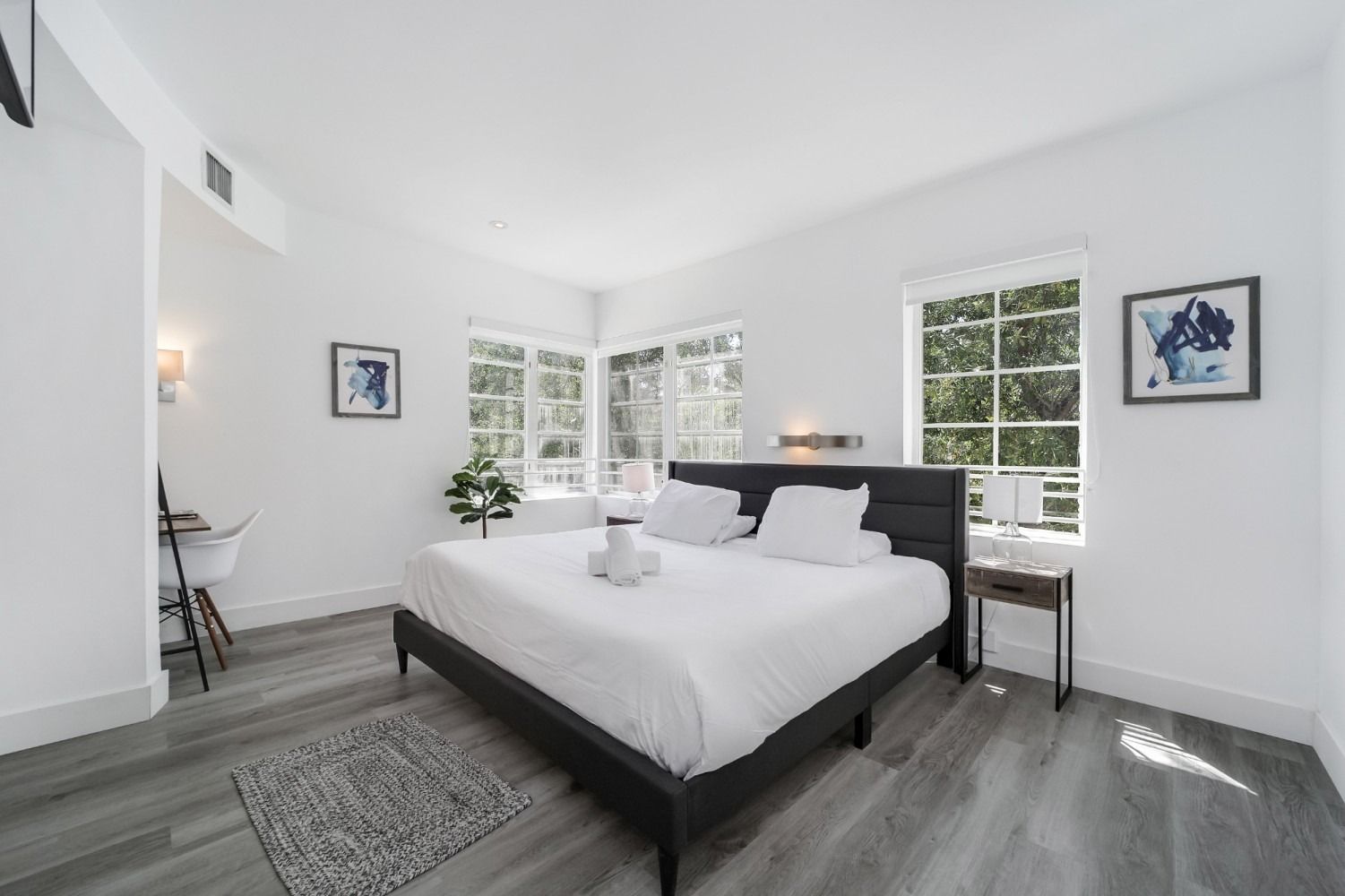 Bedroom with a king bed, white walls, and a view through the windows.