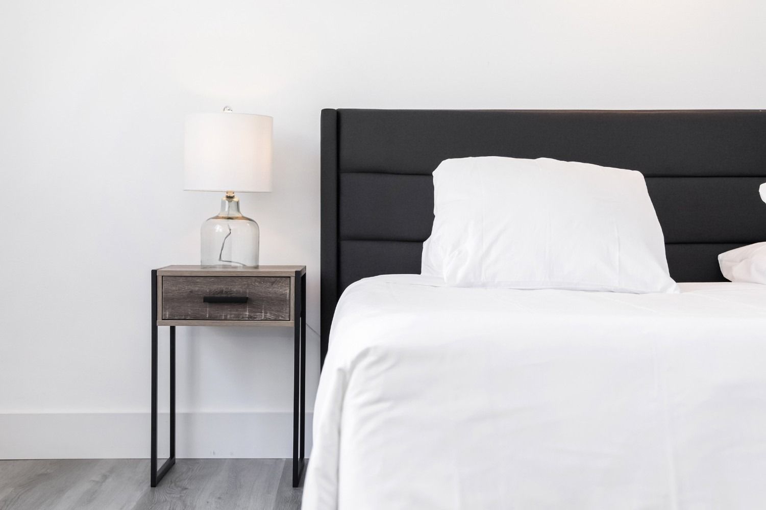 Bedroom with white bedding, black headboard, wooden nightstand, and lamp.