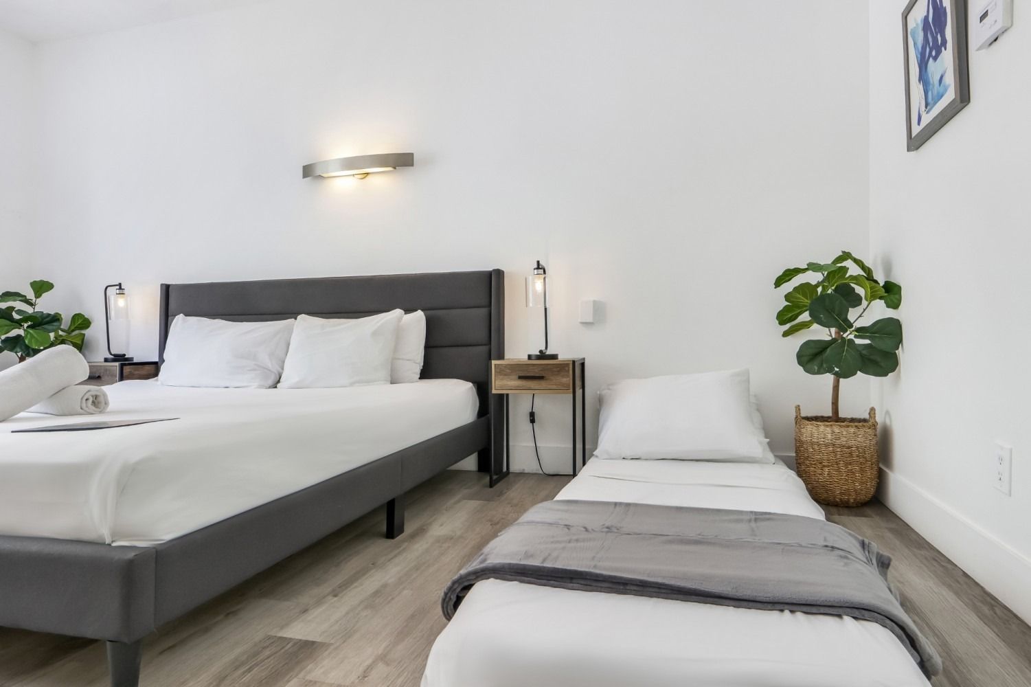 Bedroom with queen bed, single rollaway bed, neutral decor, and plants.