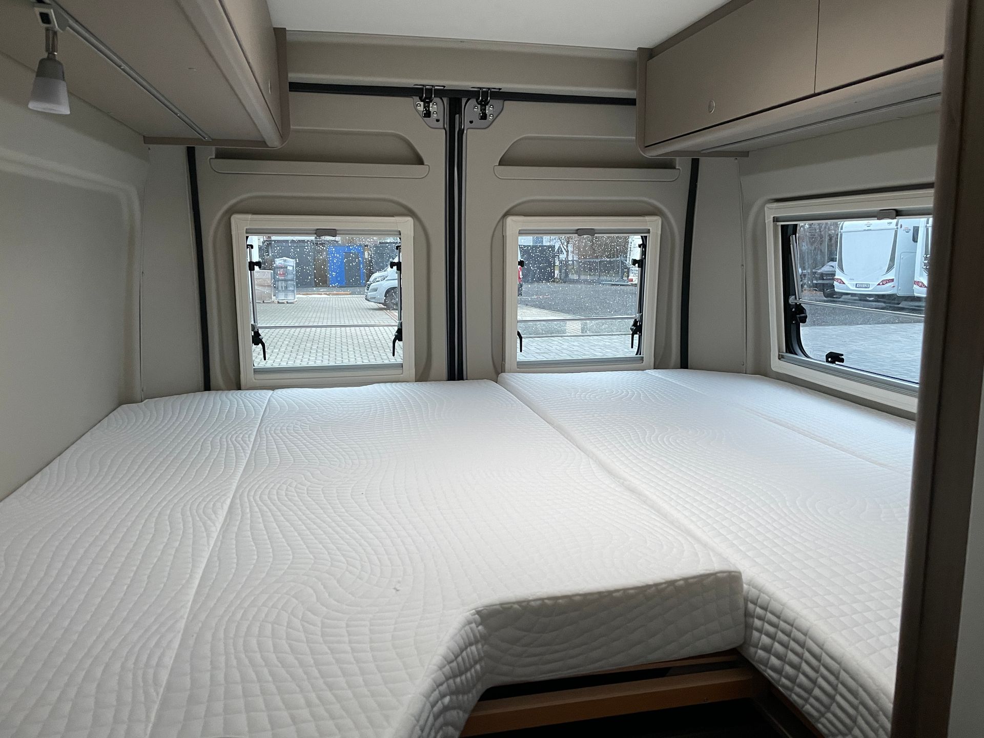 Ein Bett in einem Van mit Matratze und zwei Fenstern