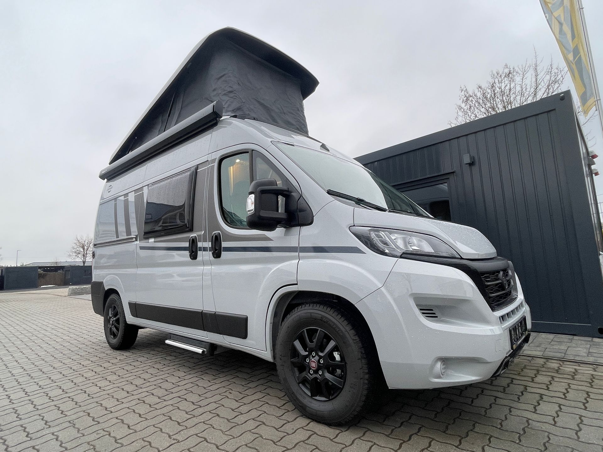 Ein weißer Lieferwagen mit schwarzem Dach steht vor einem Gebäude.