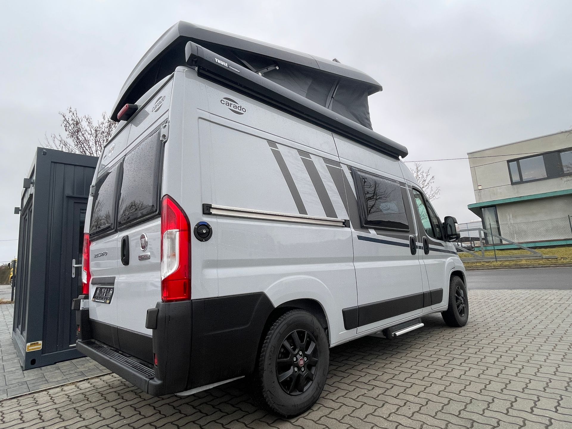 Ein weißer Lieferwagen mit Aufstelldach ist auf einem gepflasterten Gehweg geparkt.