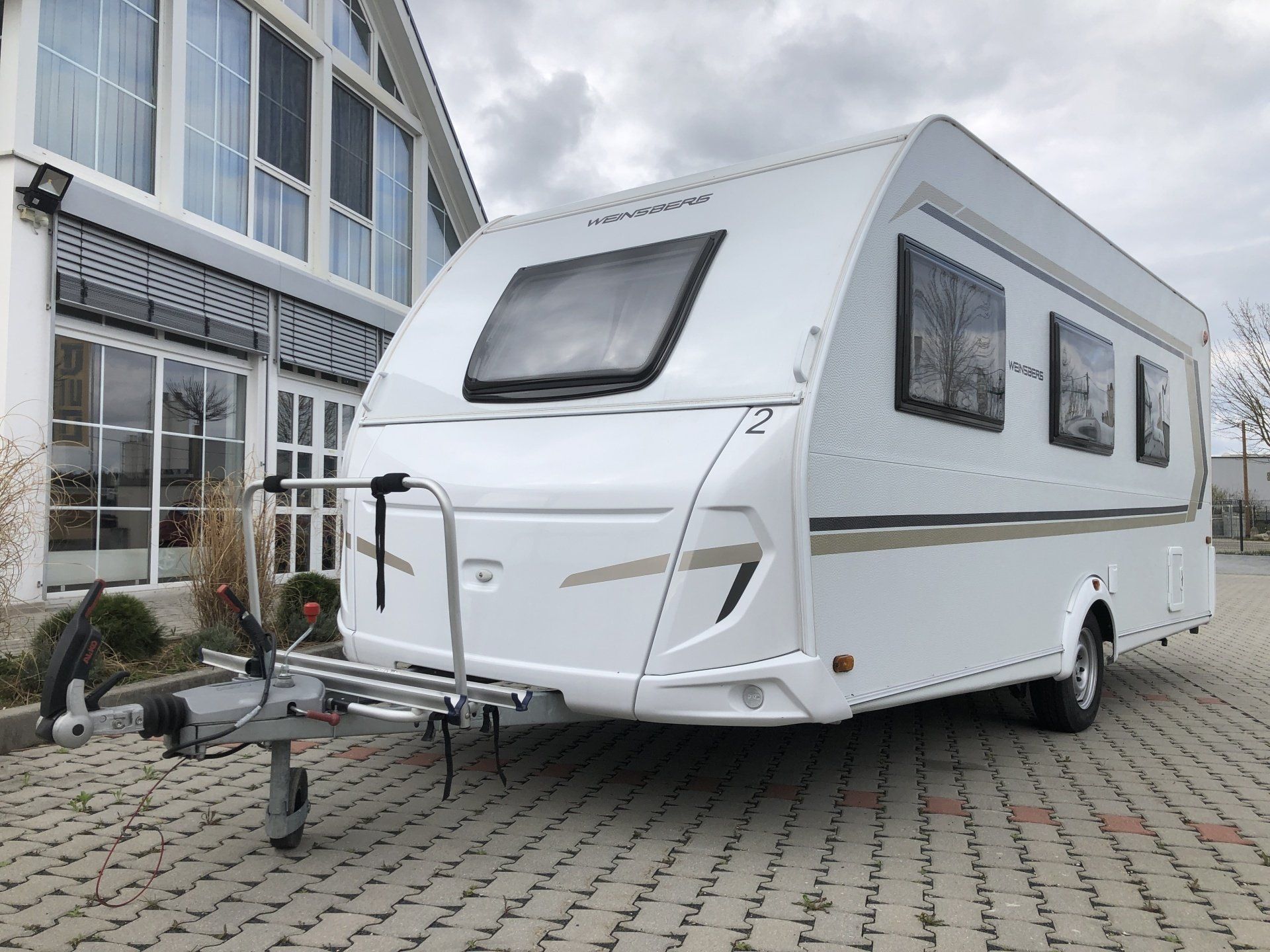A white camper trailer is parked in front of a building.