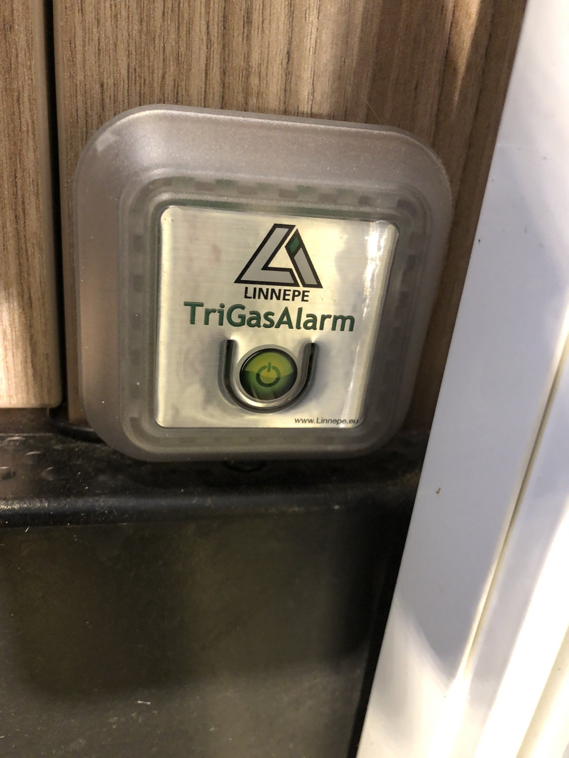 Ein Trigas-Alarm sitzt an einer Holzwand neben einer Tür.