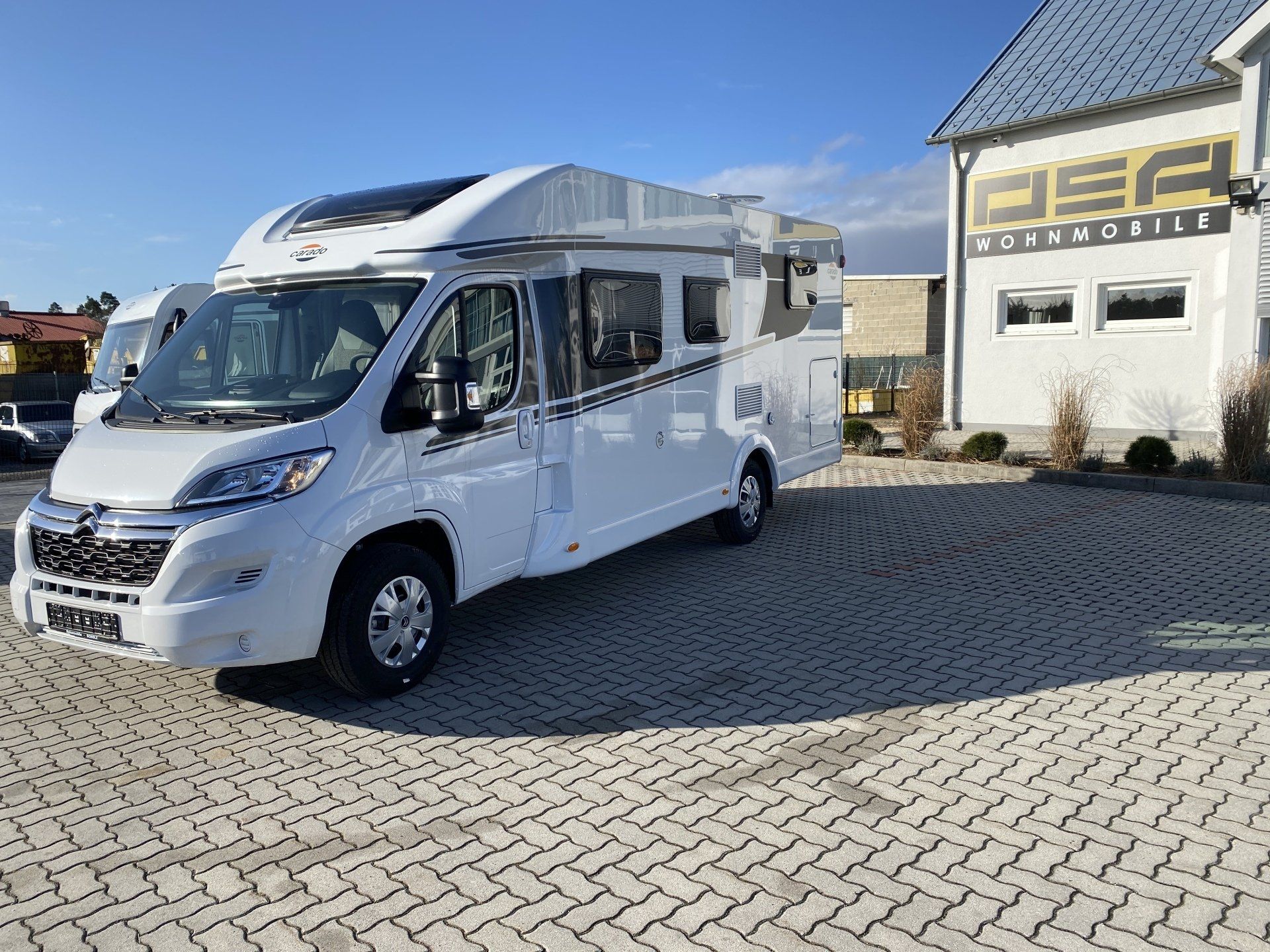 Ein weißes Wohnmobil steht auf einem Parkplatz vor einem Gebäude.