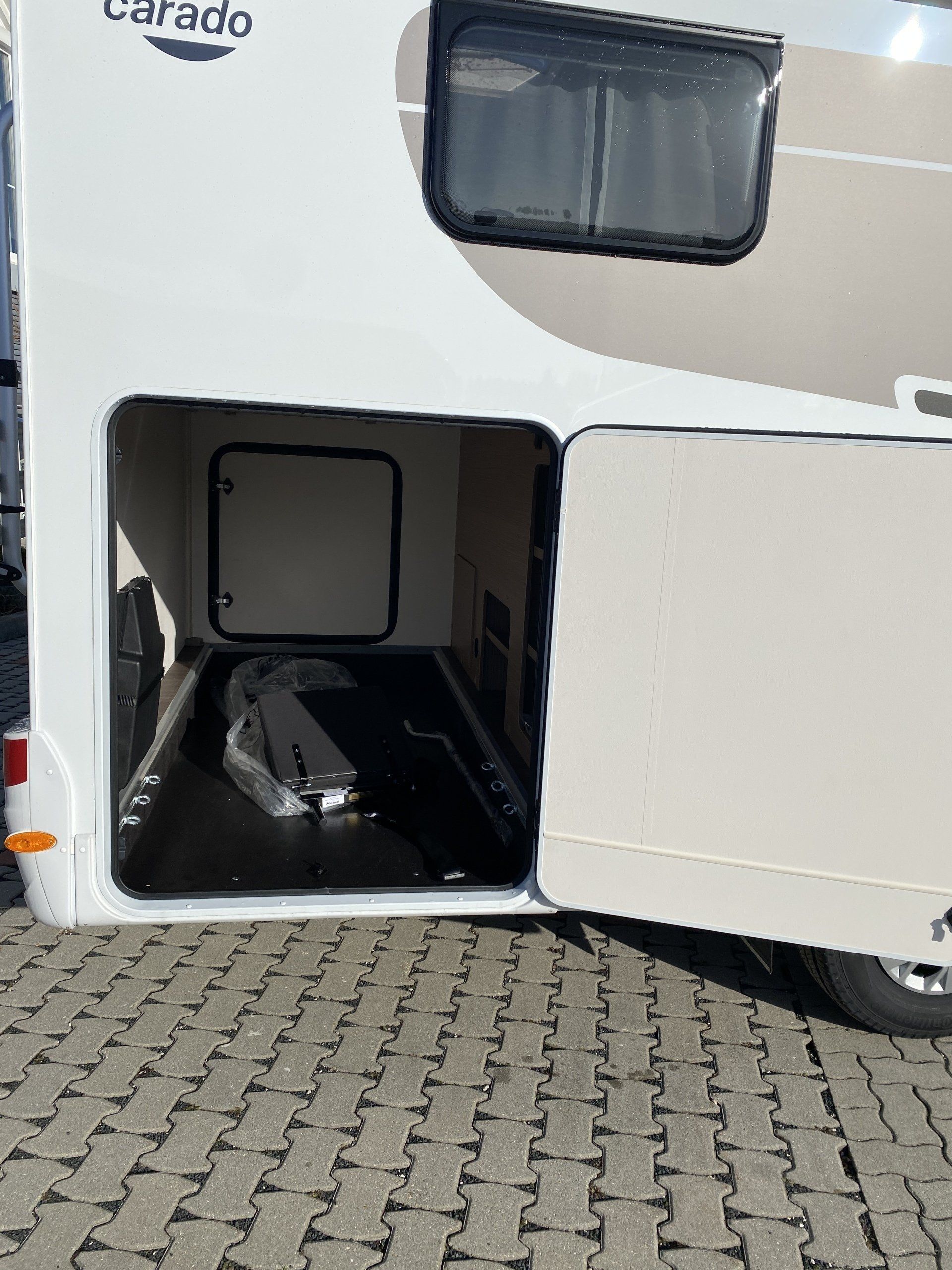 Ein weißes Wohnmobil steht mit offener Tür auf einem gepflasterten Gehweg.