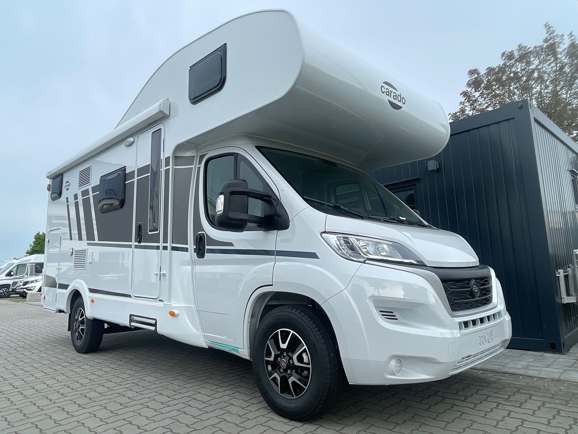 Ein weißes Wohnmobil steht vor einem schwarzen Gebäude.