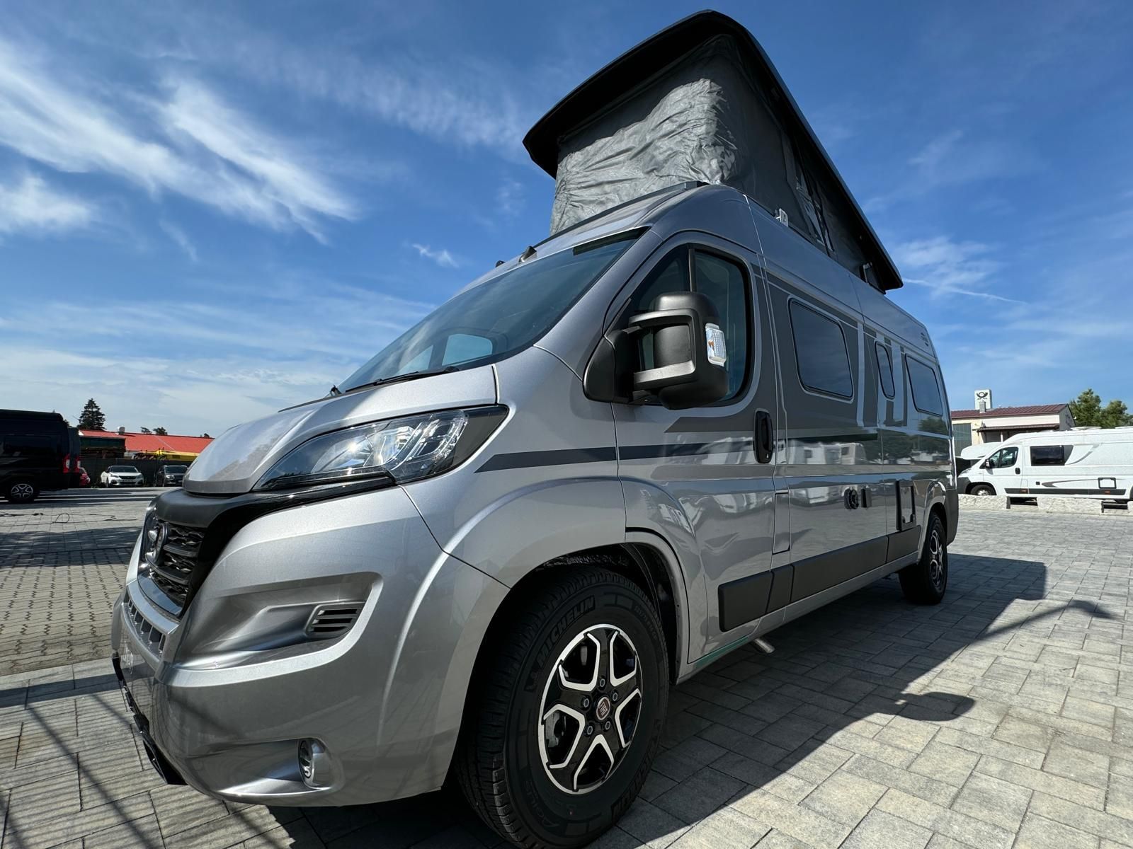 Silberner Campervan mit Aufstelldach parkt an einem sonnigen Tag draußen.
