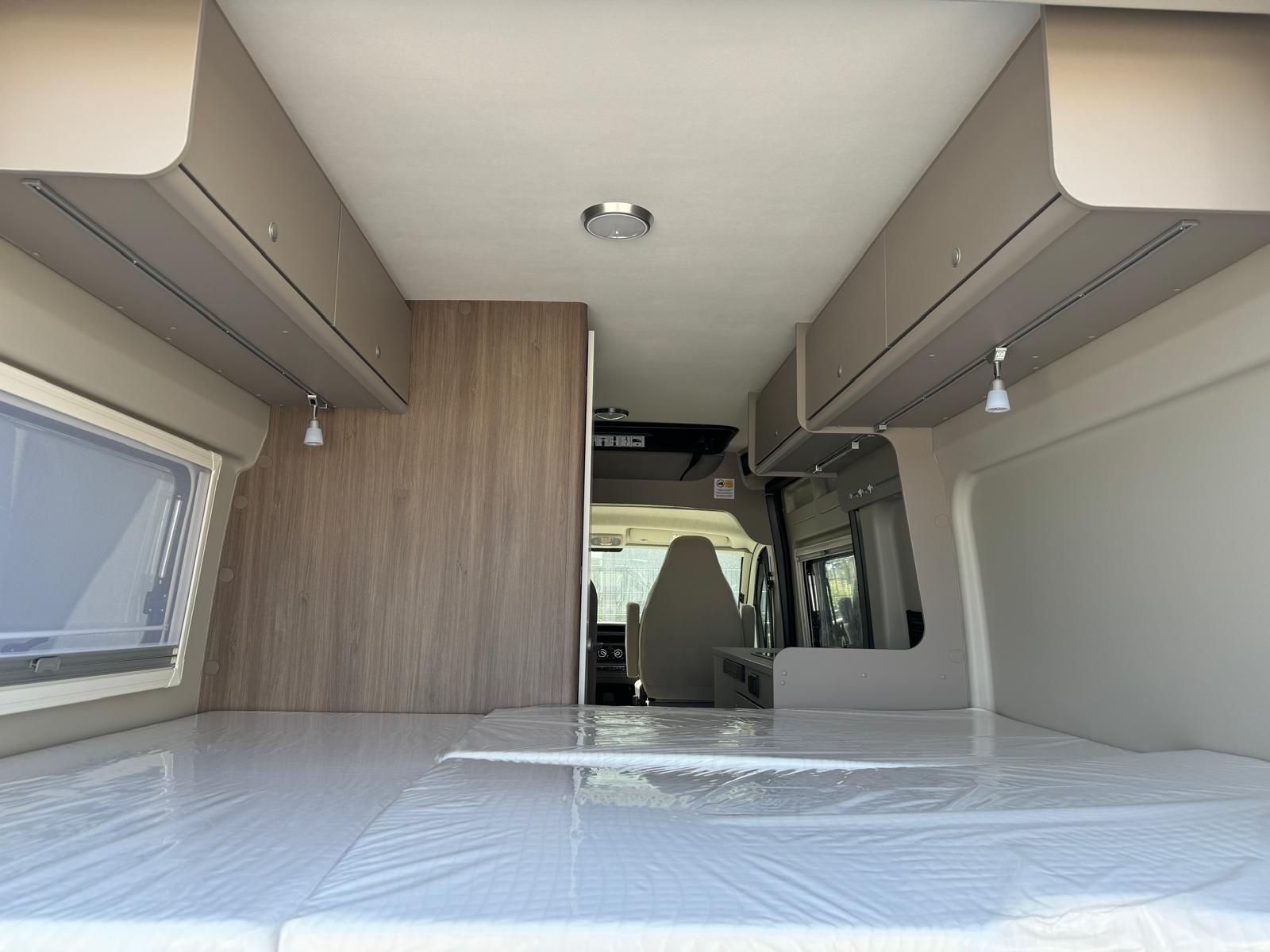 Innenansicht eines Wohnmobils mit Bett, Stauraum über den Sitzen und Blick auf den Fahrersitz.