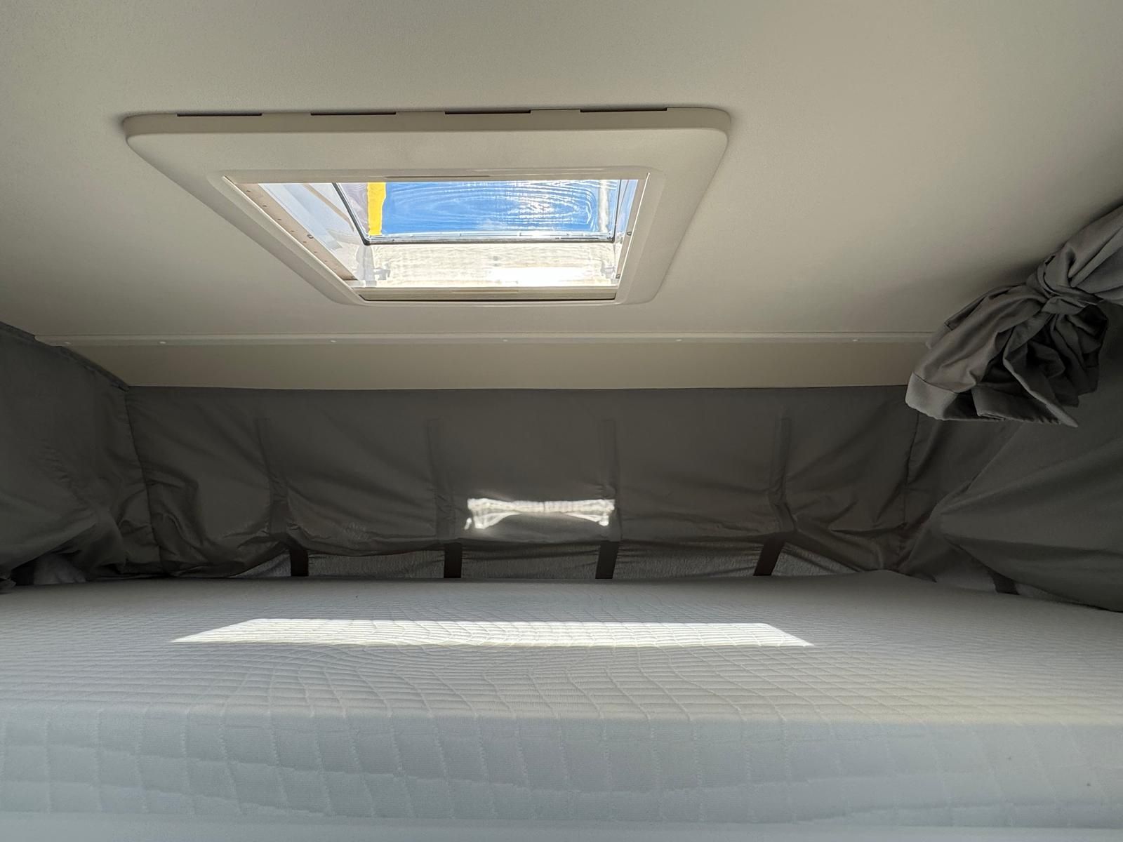 Ein Bett mit einem Oberlicht darüber in einem Wohnmobil.
