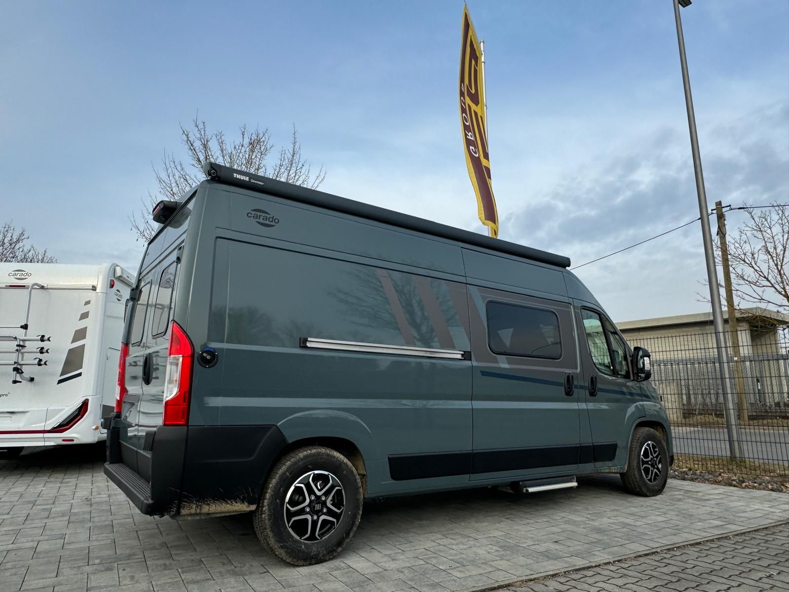 Ein dunkelgrauer Campervan parkt an einem bewölkten Tag im Freien.